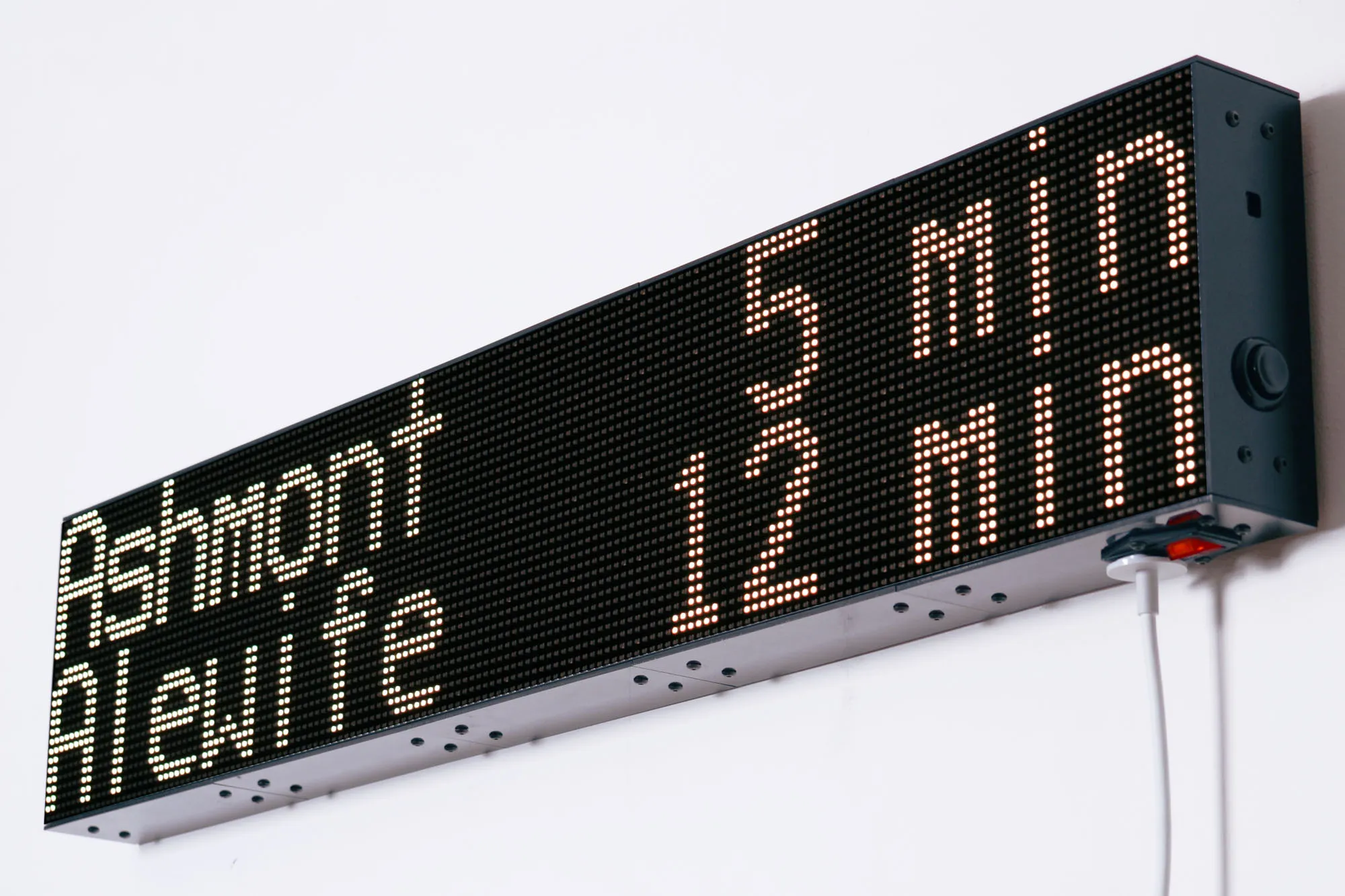 A dot-matrix headsign for the MBTA Red Line, Reading "Ashmont 5 min / Alewife 12 min"